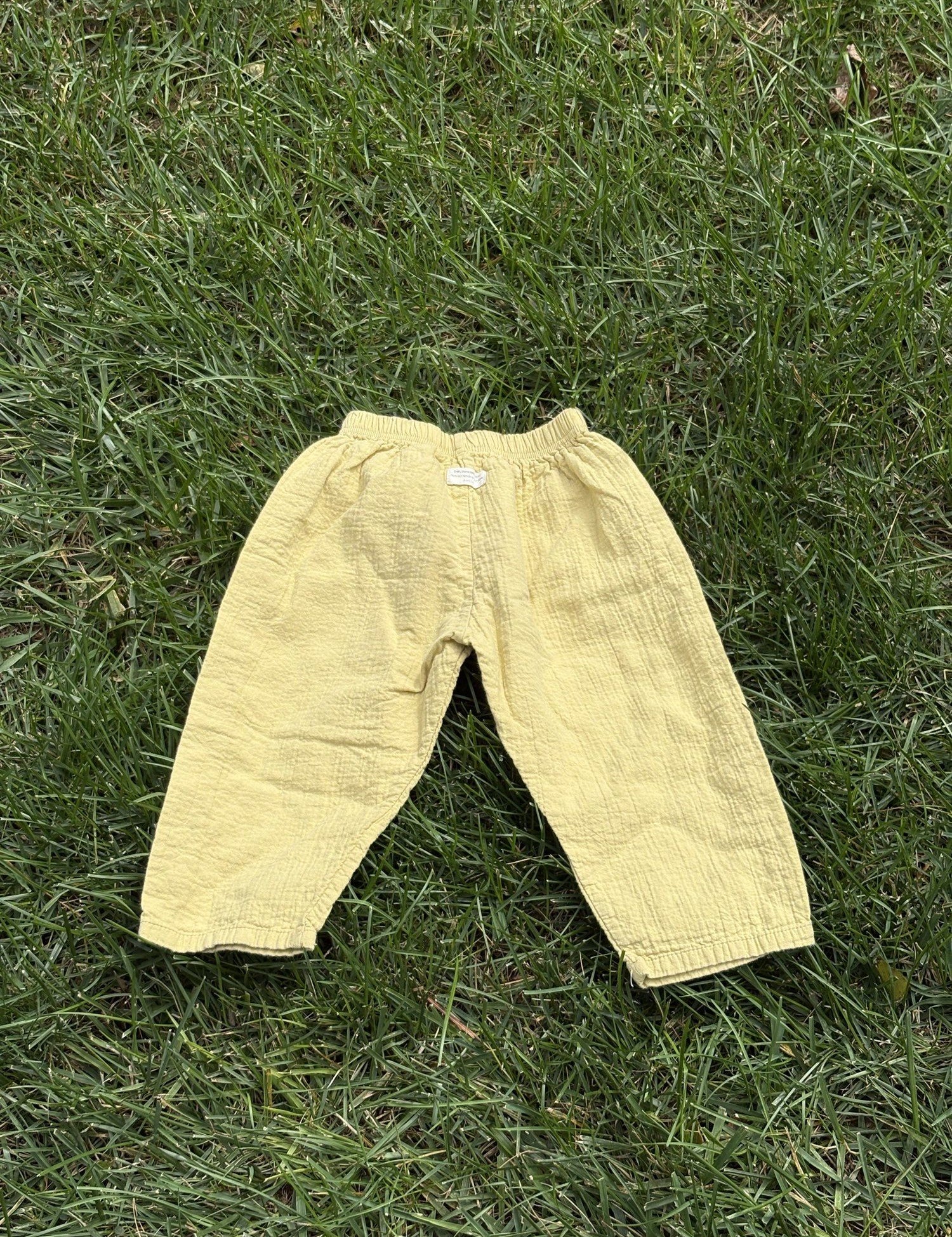 Pre-loved Aosta butter yellow cotton gauze pull-on pants, kids size 2T, back view, laid flat on grass