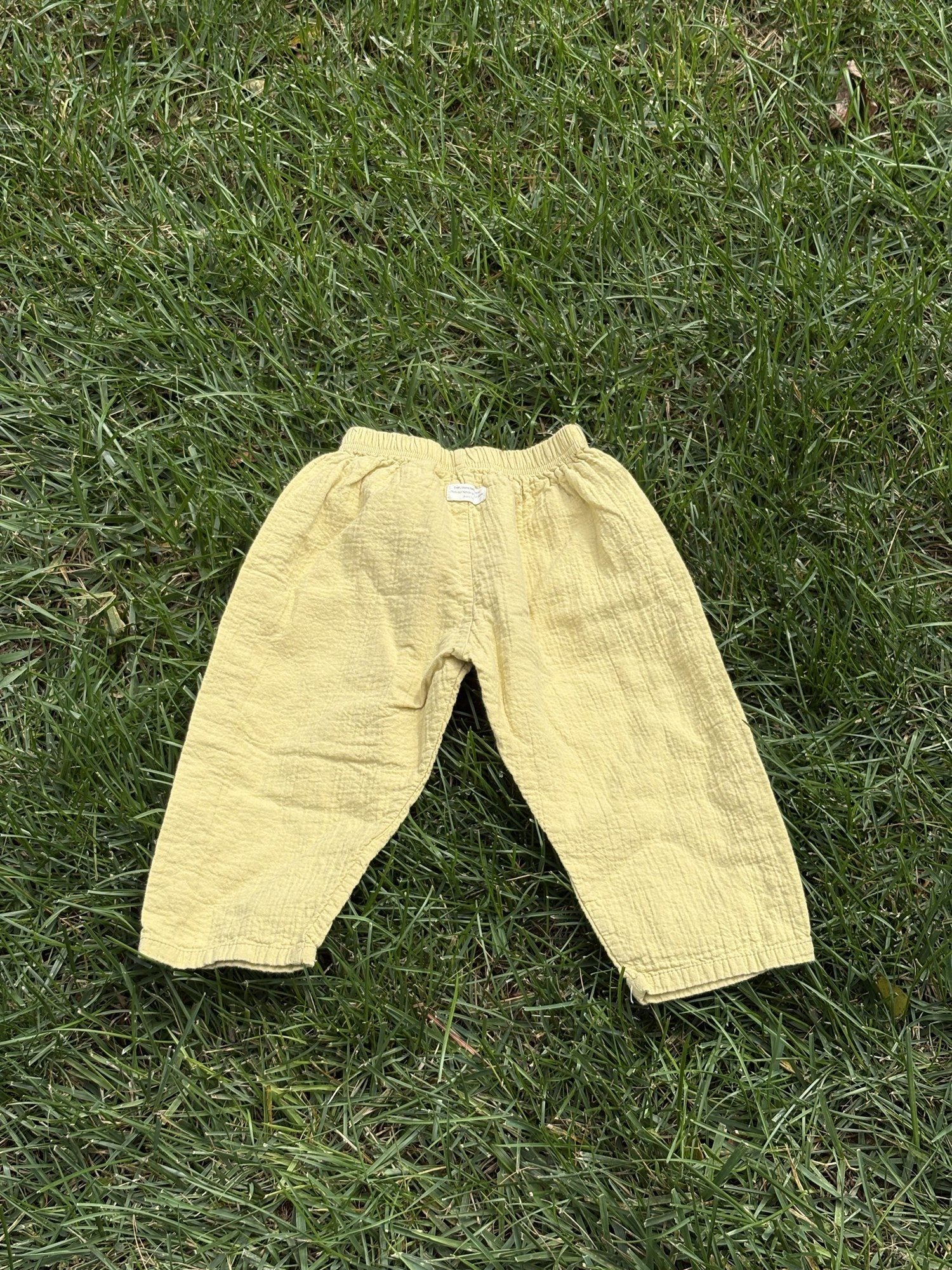 Pre-loved Aosta butter yellow cotton gauze pull-on pants, kids size 2T, back view, laid flat on grass