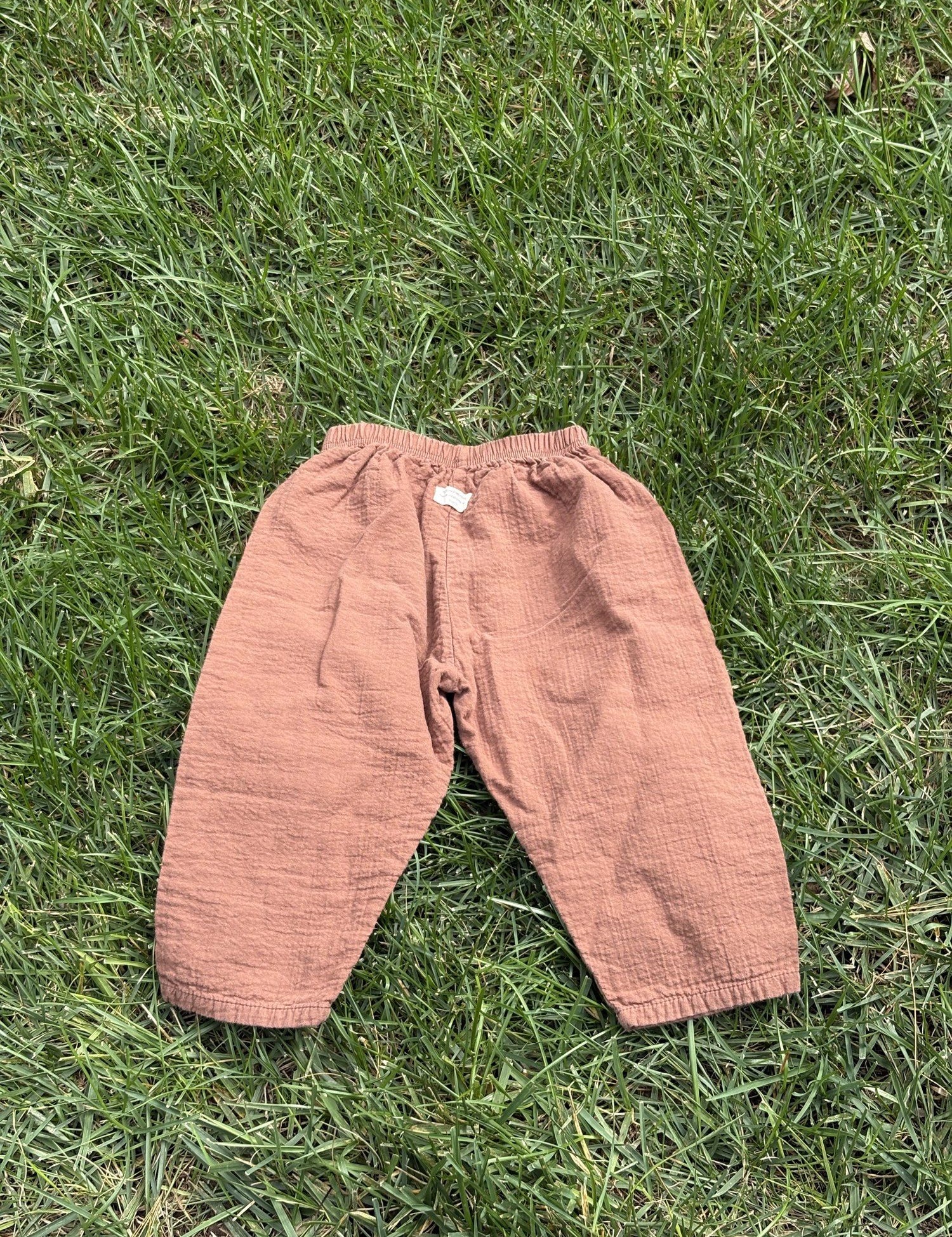Pre-loved Aosta rust cotton gauze pull-on pants, kids size 2T, back view, laid flat on grass
