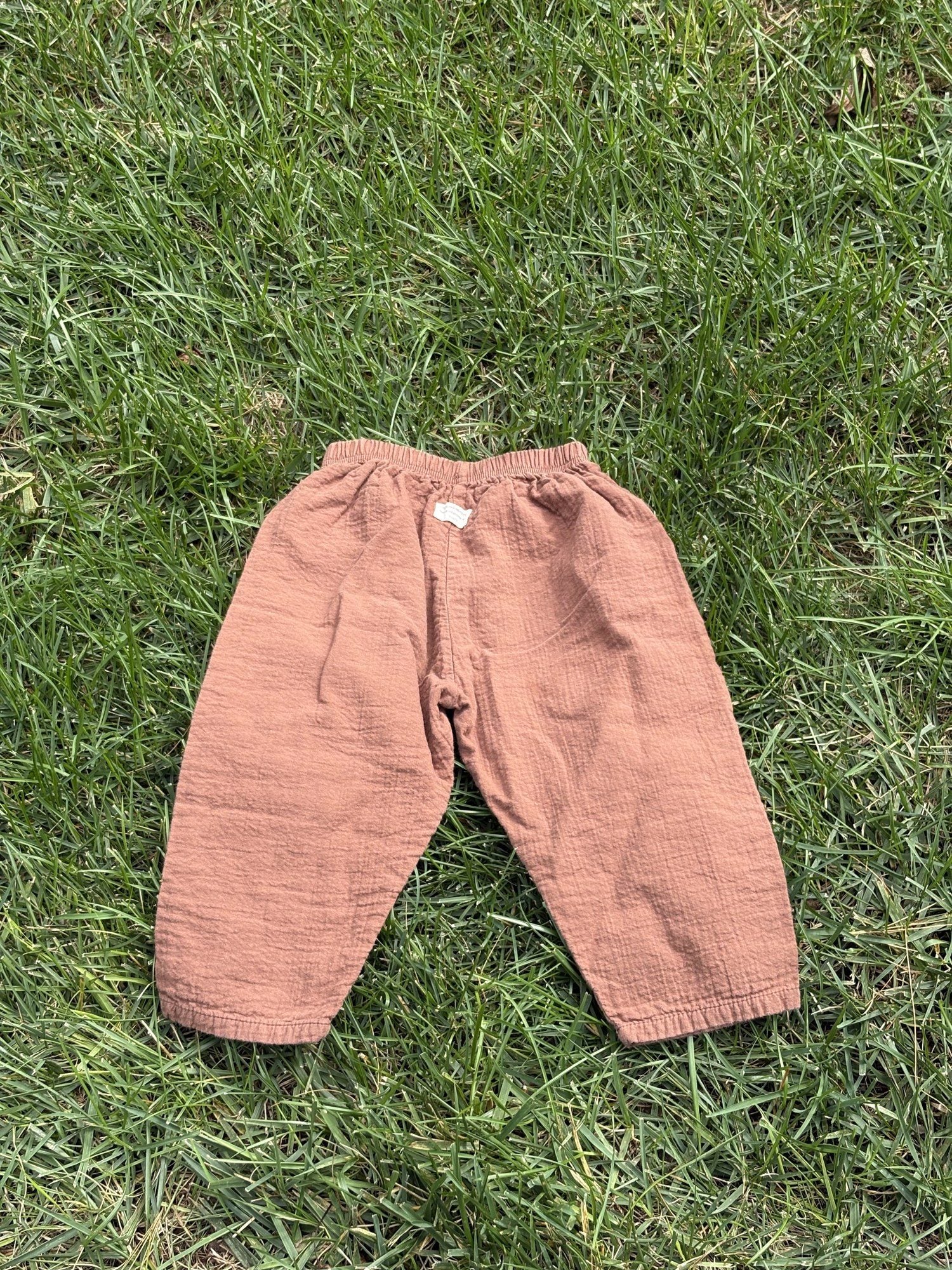 Pre-loved Aosta rust cotton gauze pull-on pants, kids size 2T, back view, laid flat on grass