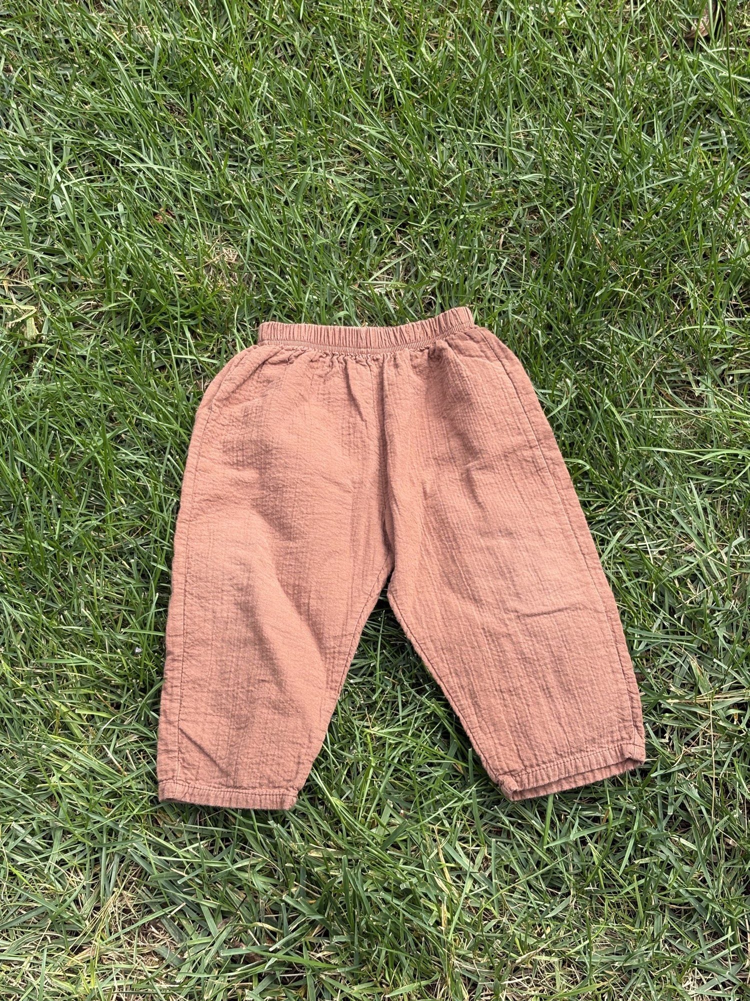 Pre-loved Aosta rust cotton gauze pull-on pants, kids size 2T, front view, laid flat on grass
