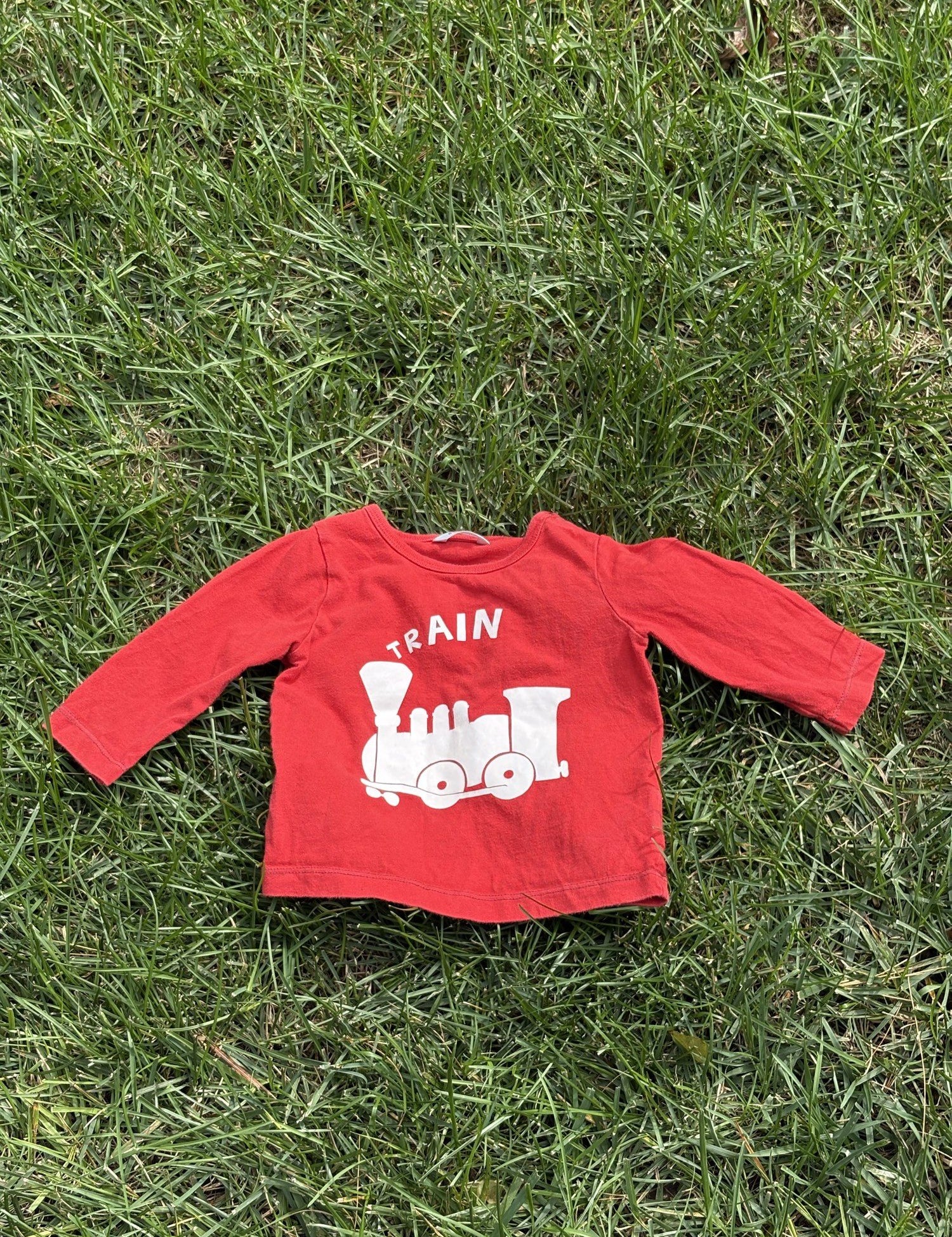 Pre-loved Boden red train graphic long-sleeve tee, kids size 6-12M, front view, laid flat on grass