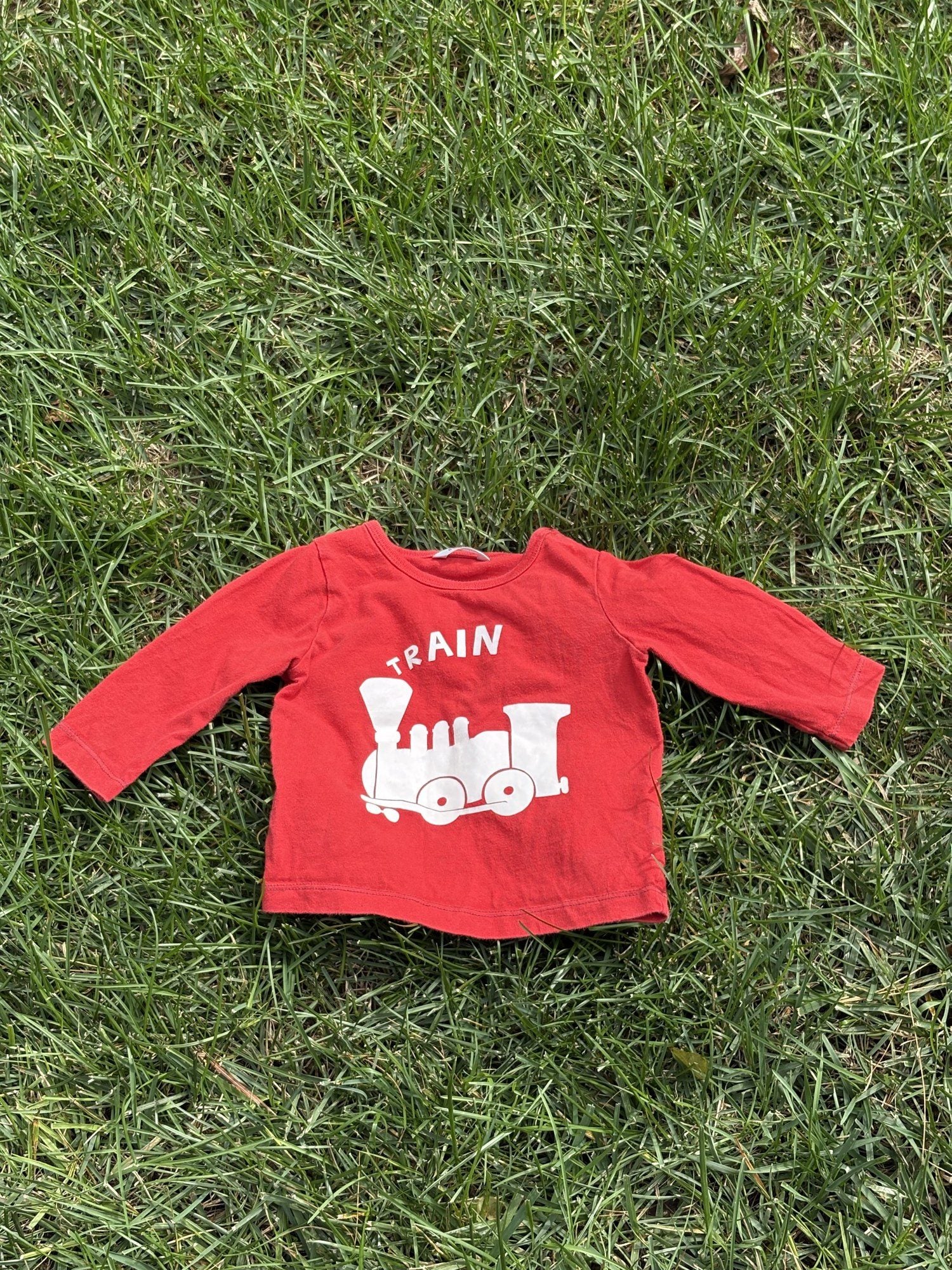 Pre-loved Boden red train graphic long-sleeve tee, kids size 6-12M, front view, laid flat on grass