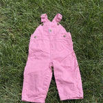 Pre-loved Carhartt pink canvas bib overalls, kids size 12M, back view, laid flat on grass