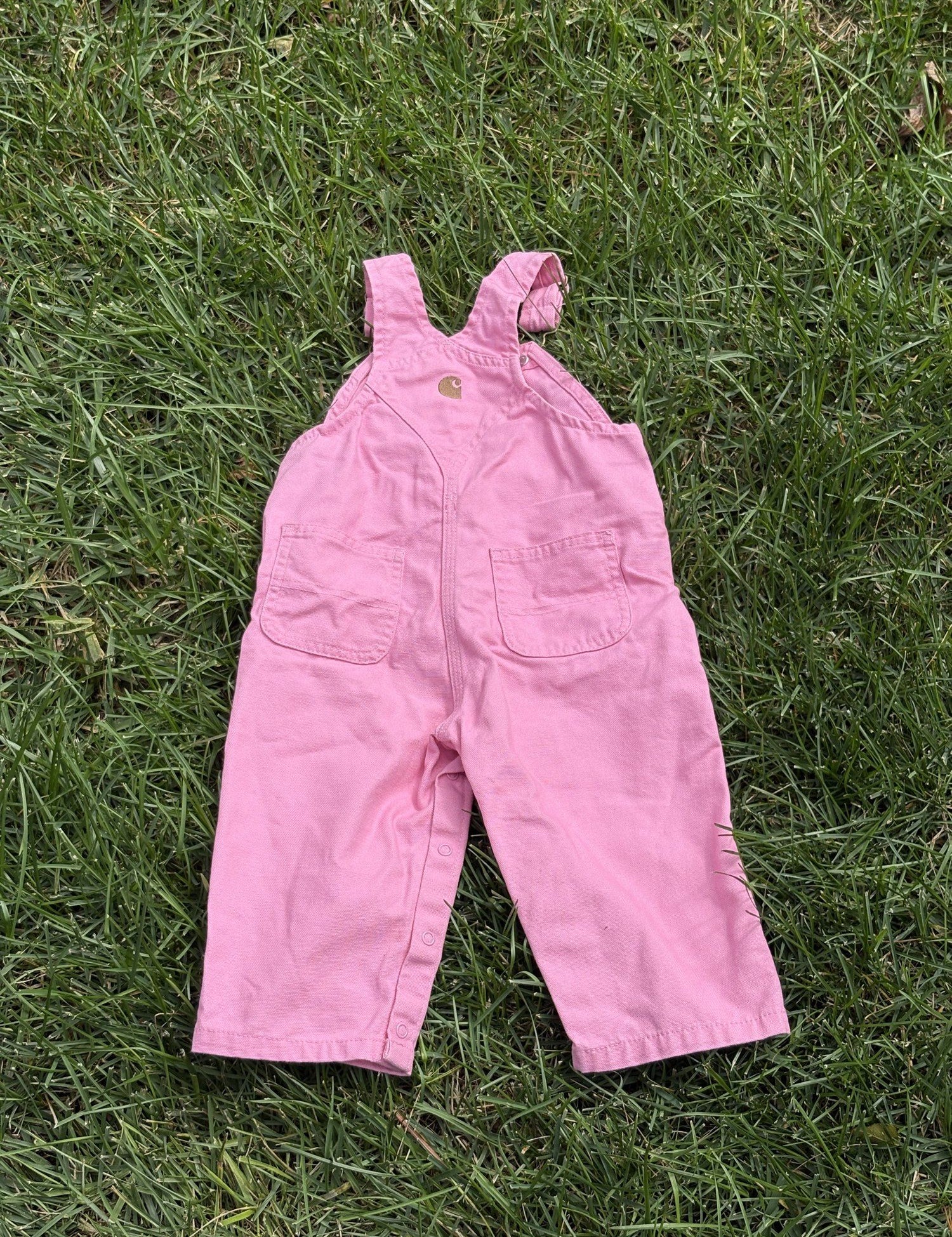 Pre-loved Carhartt pink canvas bib overalls, kids size 12M, front view, laid flat on grass