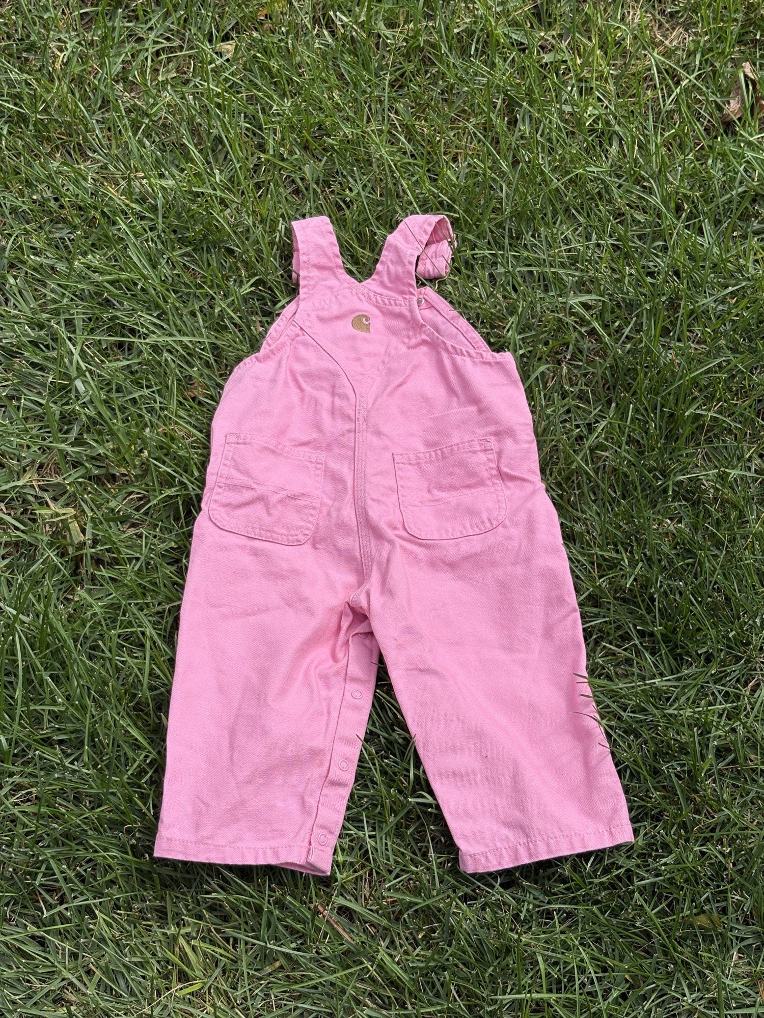 Pre-loved Carhartt pink canvas bib overalls, kids size 12M, front view, laid flat on grass