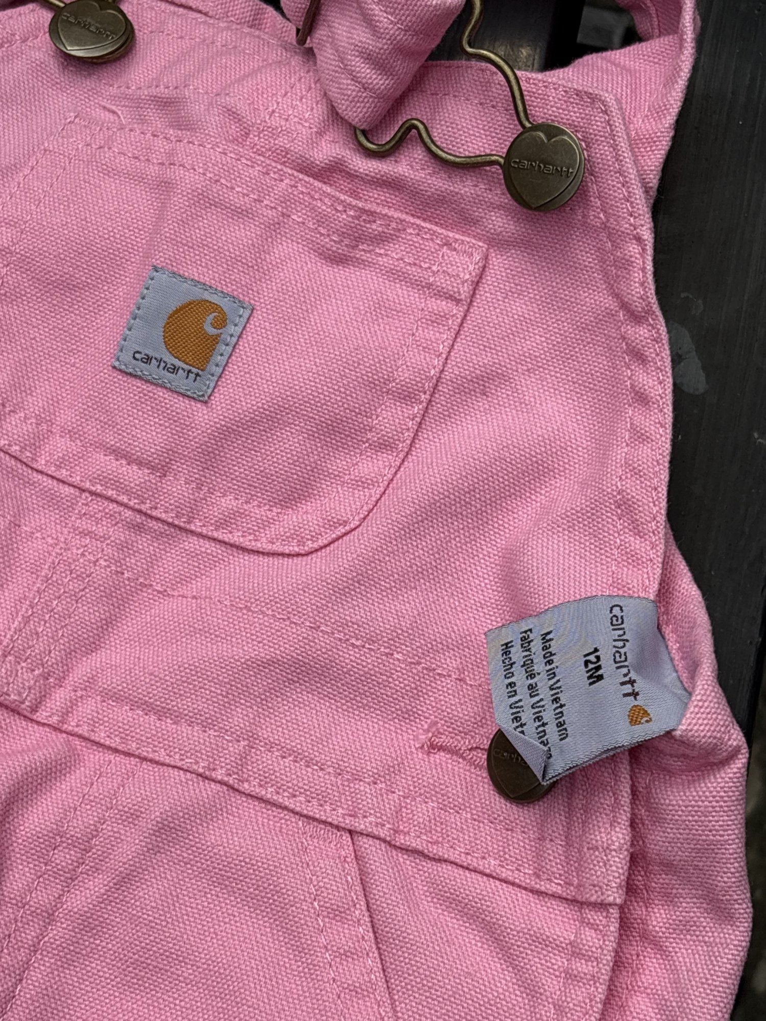 Pre-loved Carhartt pink canvas bib overalls, kids size 12M, brand and size label close-up