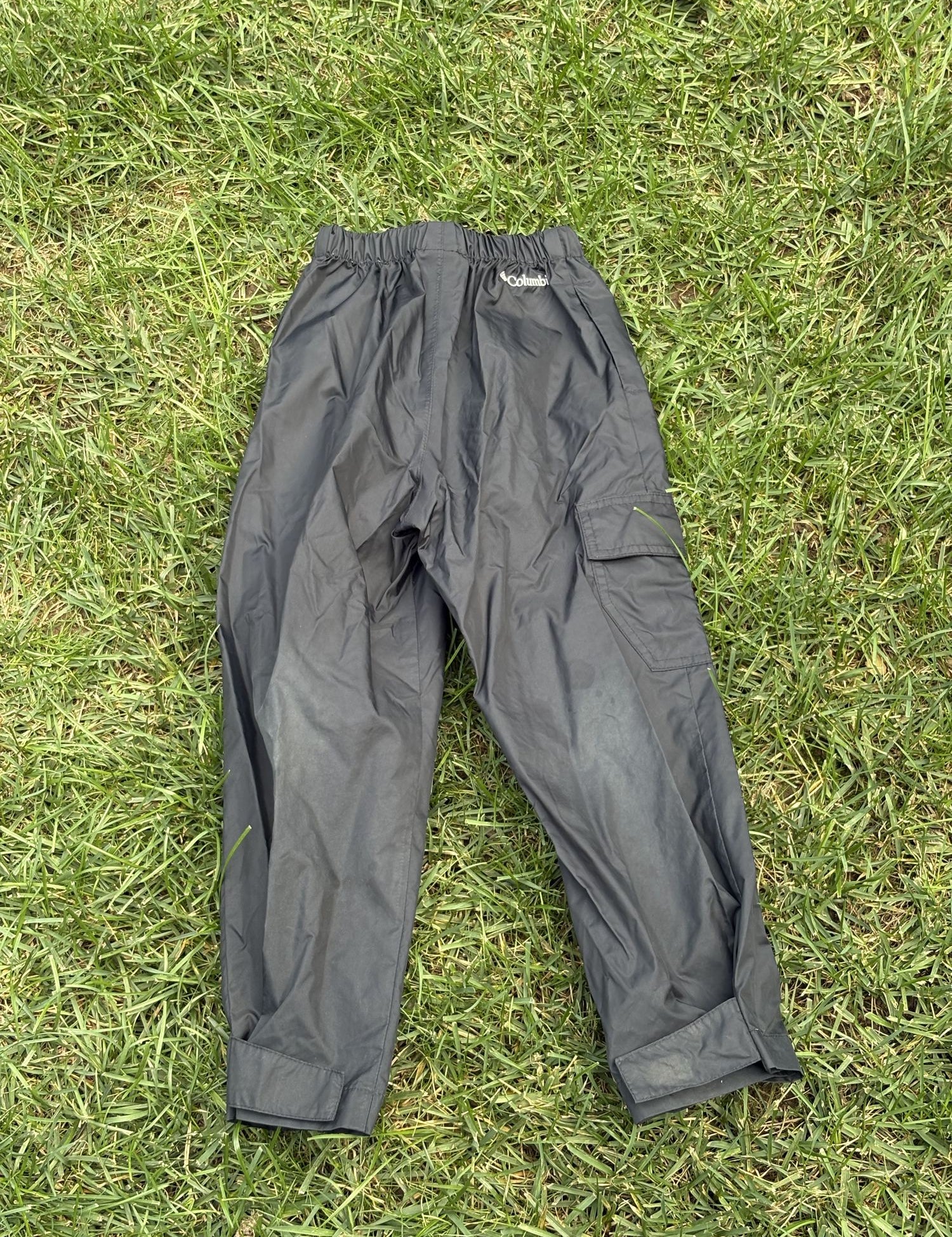 Pre-loved Columbia black pull-on rain pants, kids size 4/5, back view, laid flat on grass