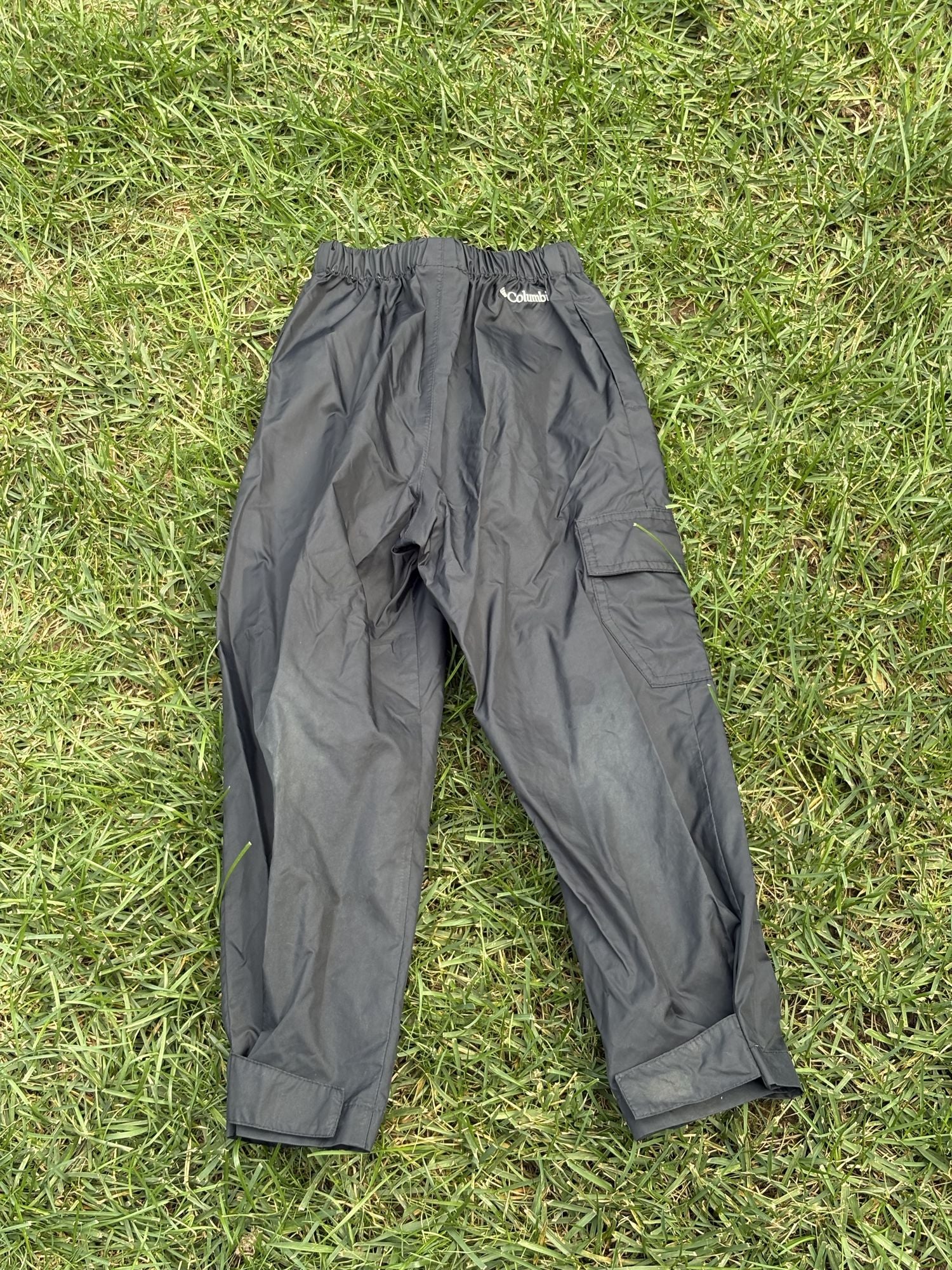 Pre-loved Columbia black pull-on rain pants, kids size 4/5, back view, laid flat on grass