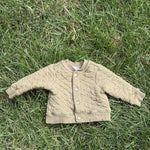 Pre-loved Hanna Andersson khaki quilted snap-front jacket, kids size 6-12M, front view, laid flat on grass