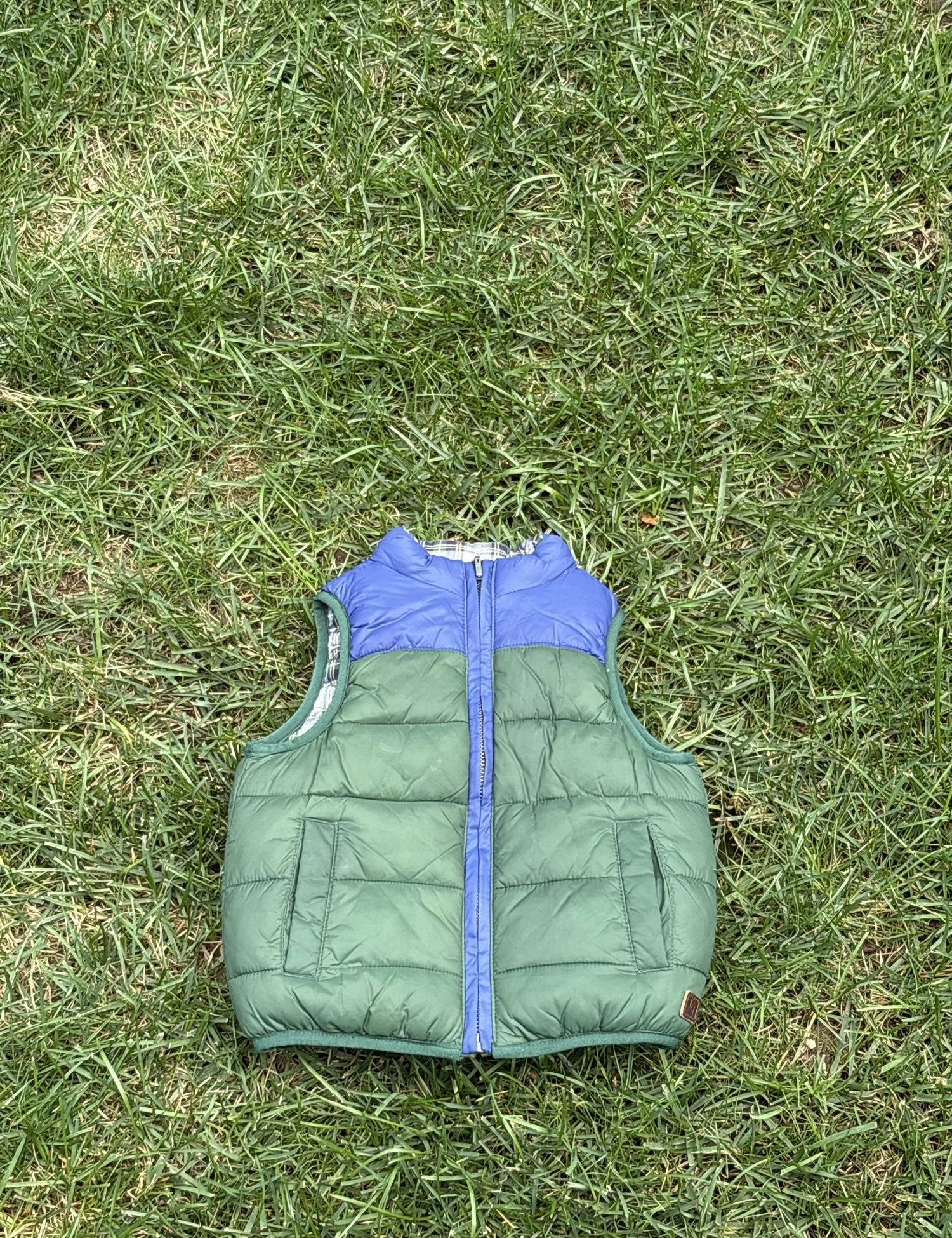 Pre-loved Janie and Jack green and blue colorblock puffer vest, kids size 18-24M, front view, laid flat on grass