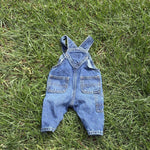 Pre-loved Old Navy denim workwear bib overalls, kids size 3-6M, back view, laid flat on grass