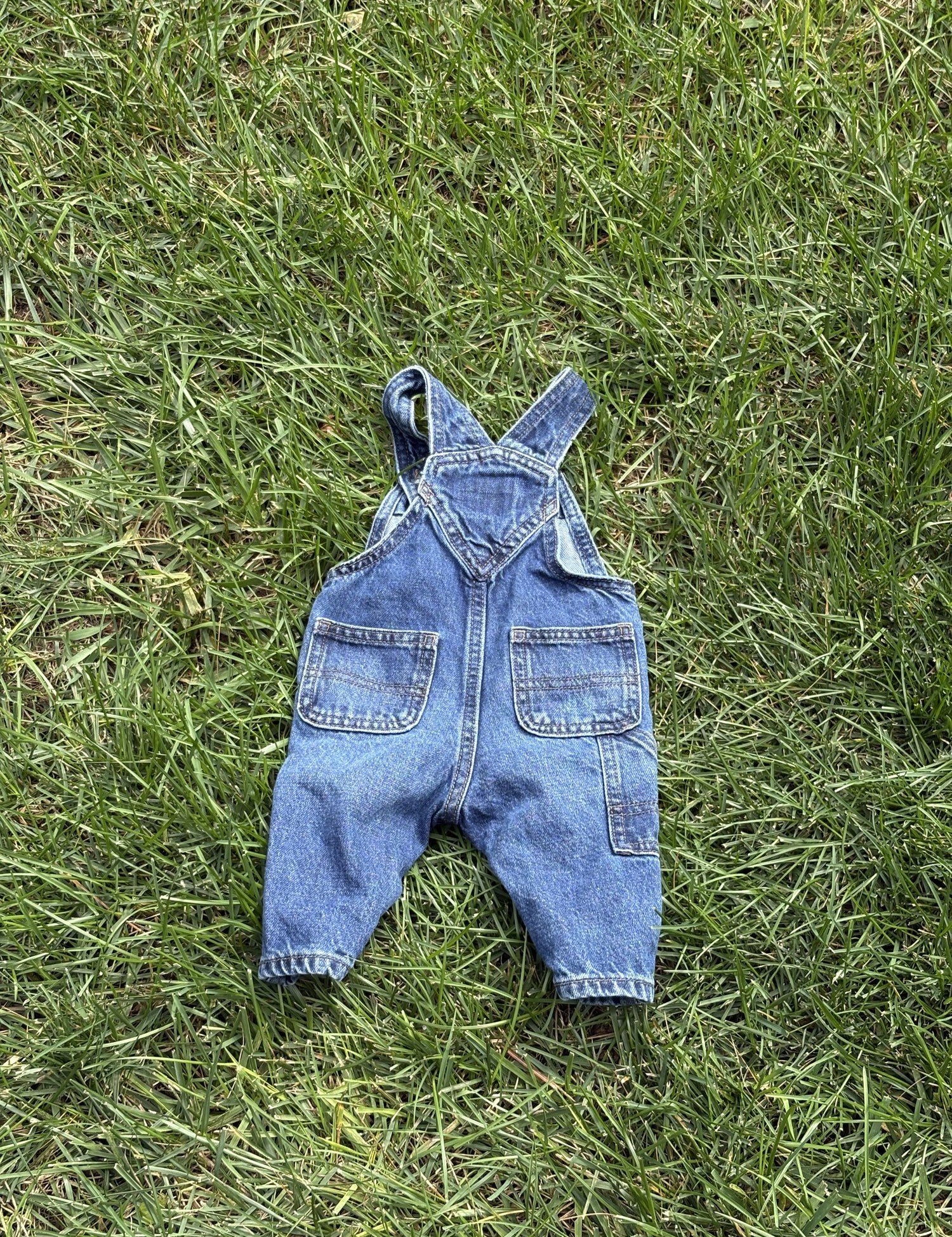 Pre-loved Old Navy denim workwear bib overalls, kids size 3-6M, back view, laid flat on grass