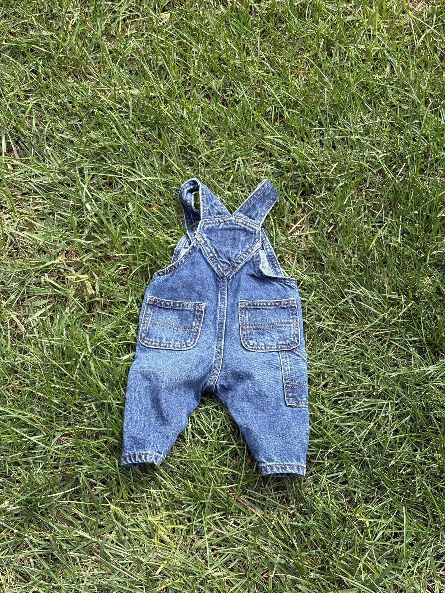 Pre-loved Old Navy denim workwear bib overalls, kids size 3-6M, back view, laid flat on grass