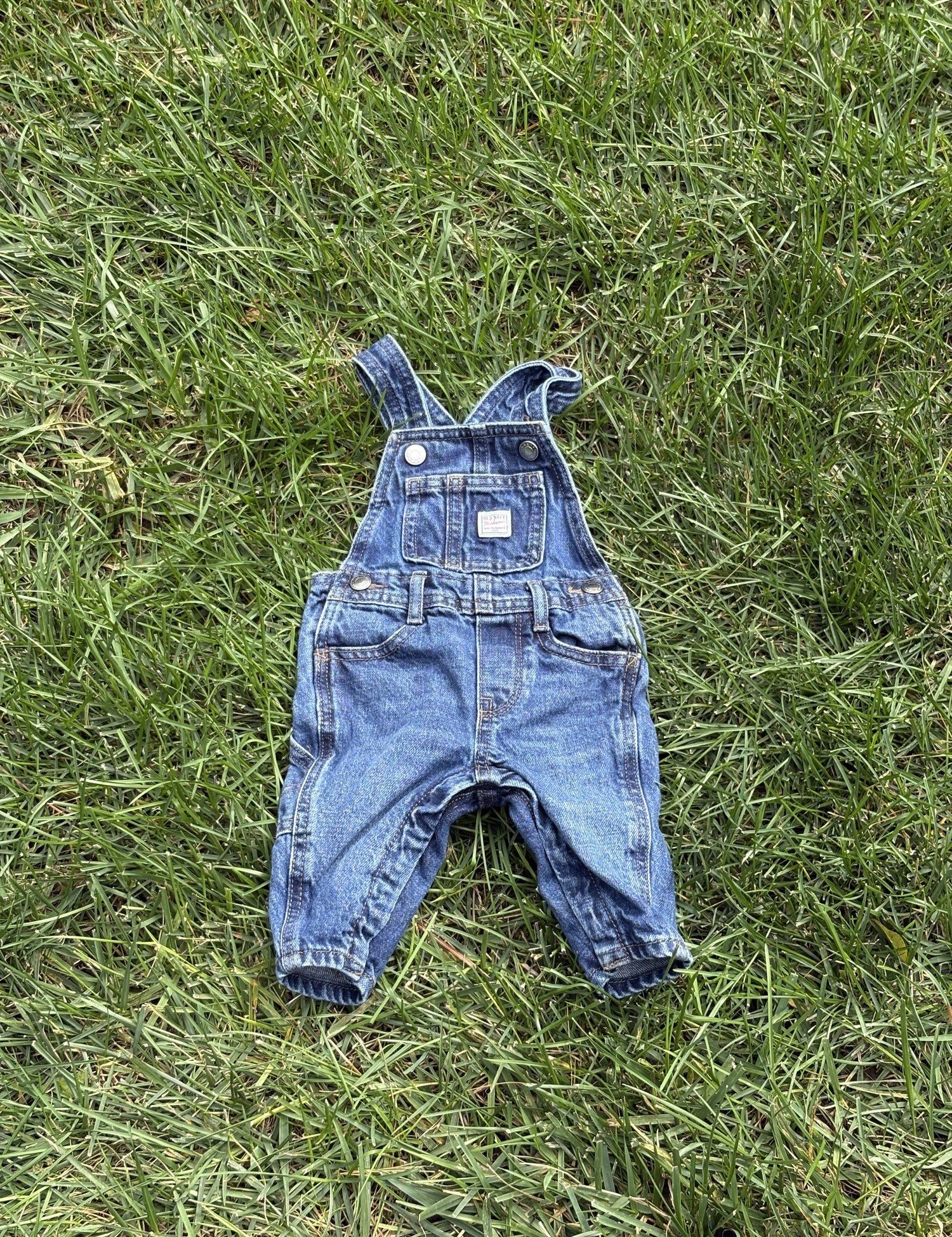 Pre-loved Old Navy denim workwear bib overalls, kids size 3-6M, front view, laid flat on grass