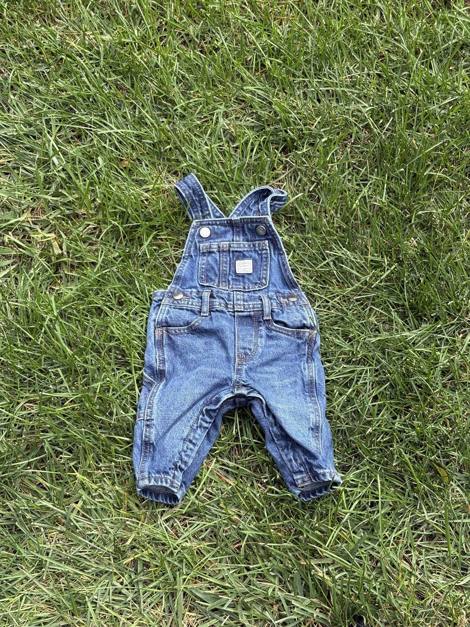 Pre-loved Old Navy denim workwear bib overalls, kids size 3-6M, front view, laid flat on grass
