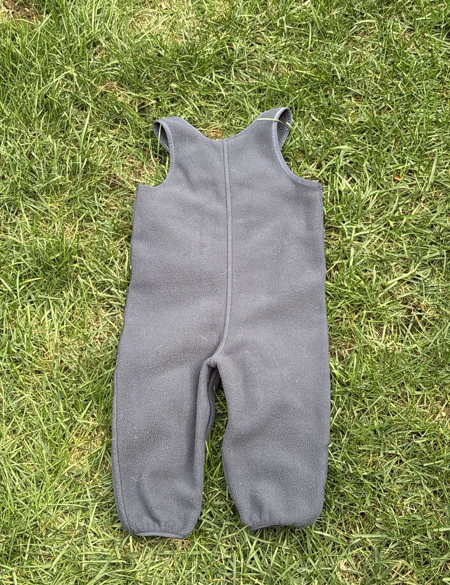 Pre-loved Patagonia charcoal fleece bib overalls, kids size 12-18M, back view, laid flat on grass