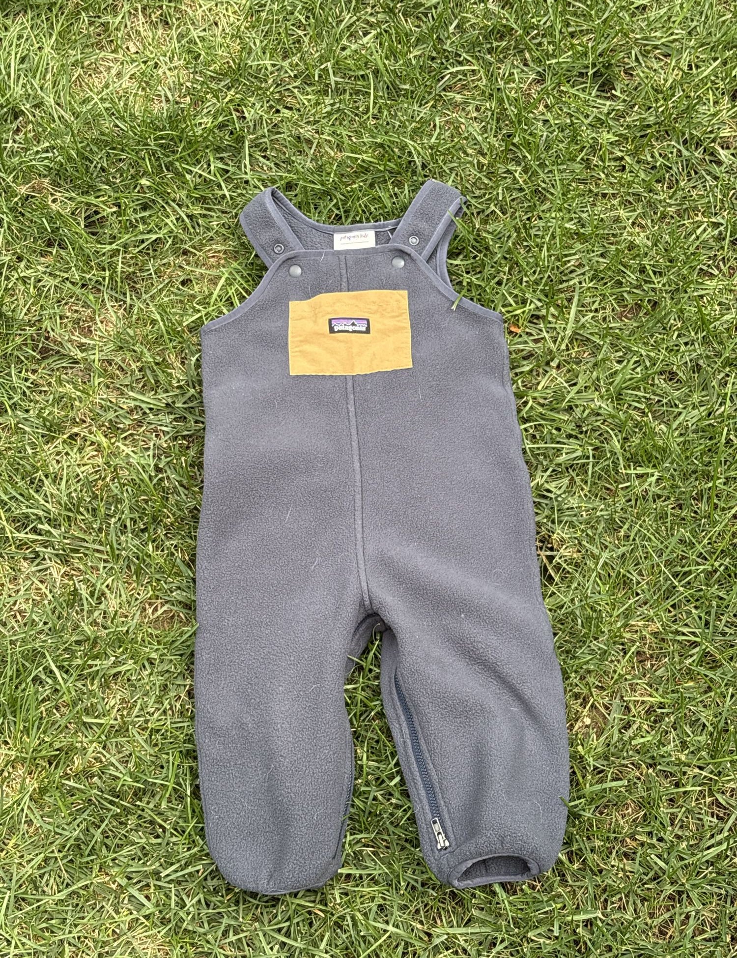 Pre-loved Patagonia charcoal fleece bib overalls, kids size 12-18M, front view, laid flat on grass