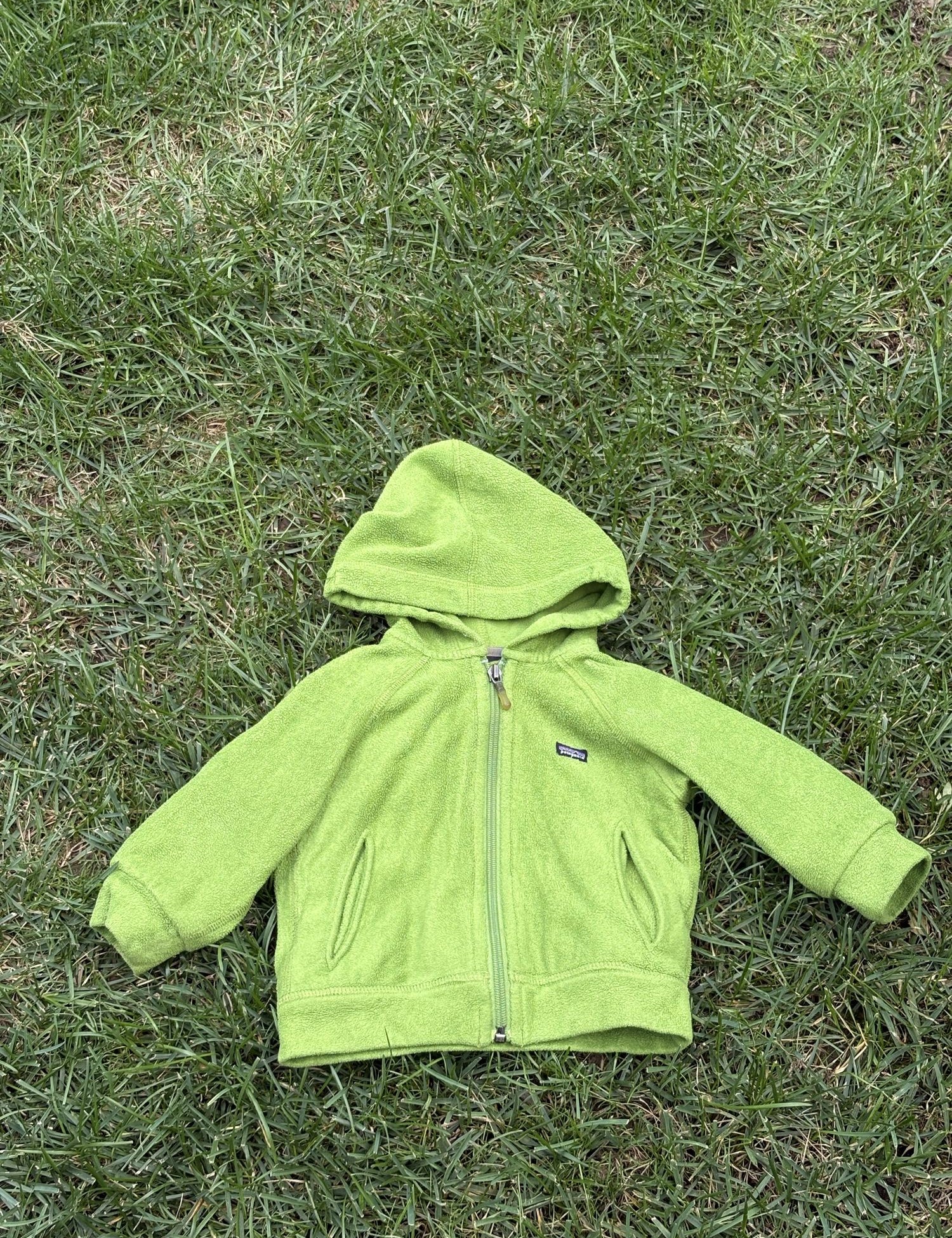 Pre-loved Patagonia green hooded full-zip fleece jacket, kids size 6M, front view, laid flat on grass