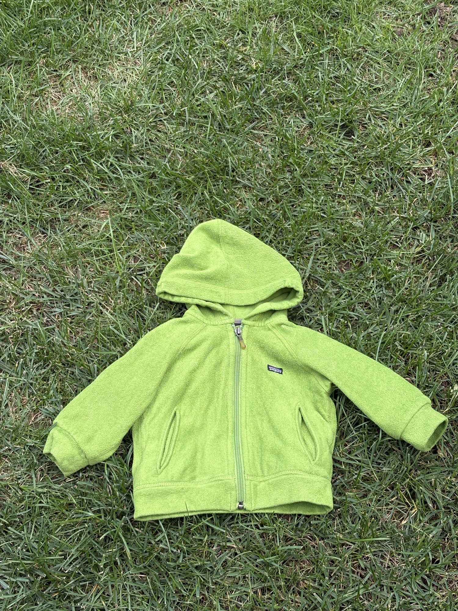 Pre-loved Patagonia green hooded full-zip fleece jacket, kids size 6M, front view, laid flat on grass
