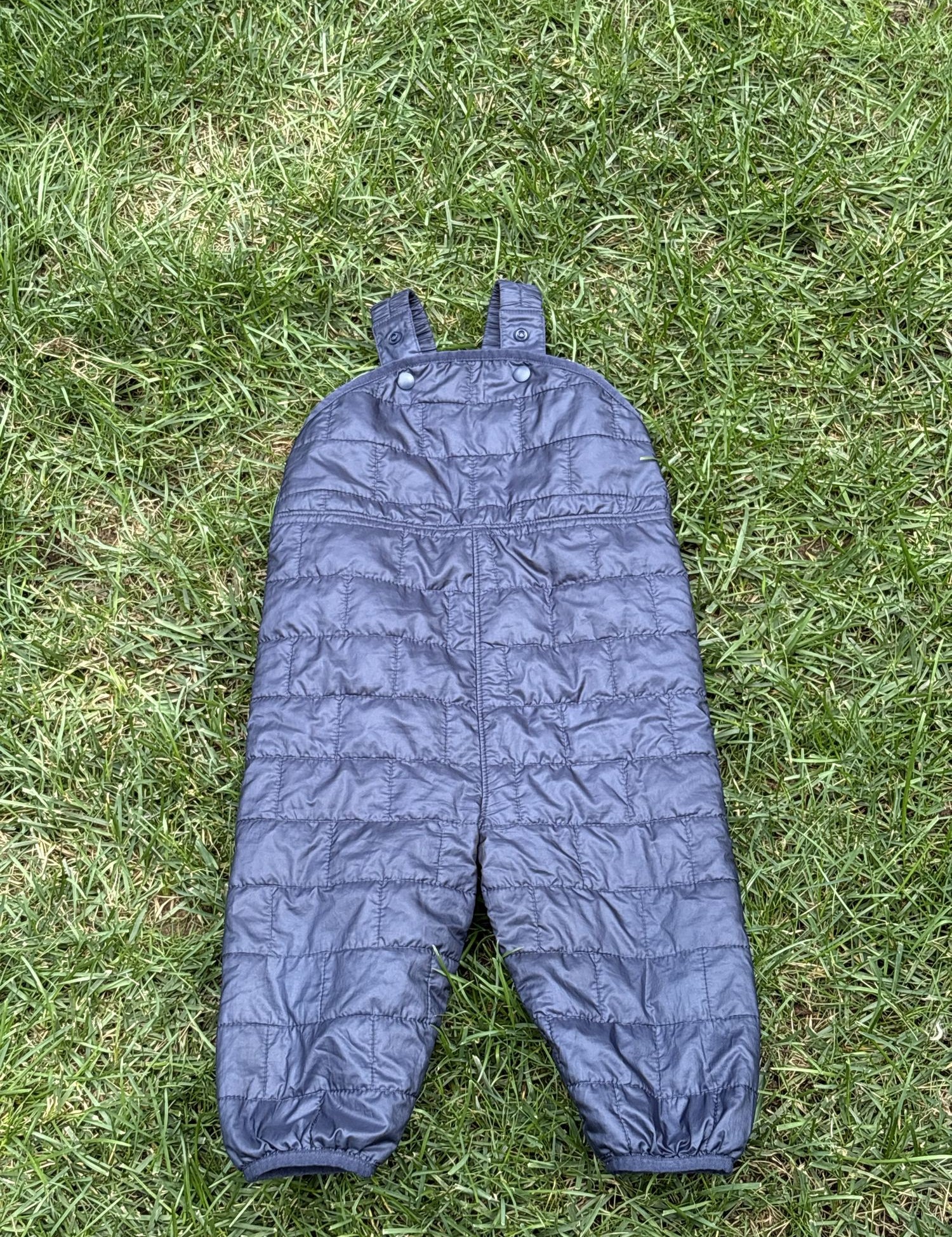 Pre-loved Patagonia navy quilted insulated bib overalls, kids size 12-18M, back view, laid flat on grass