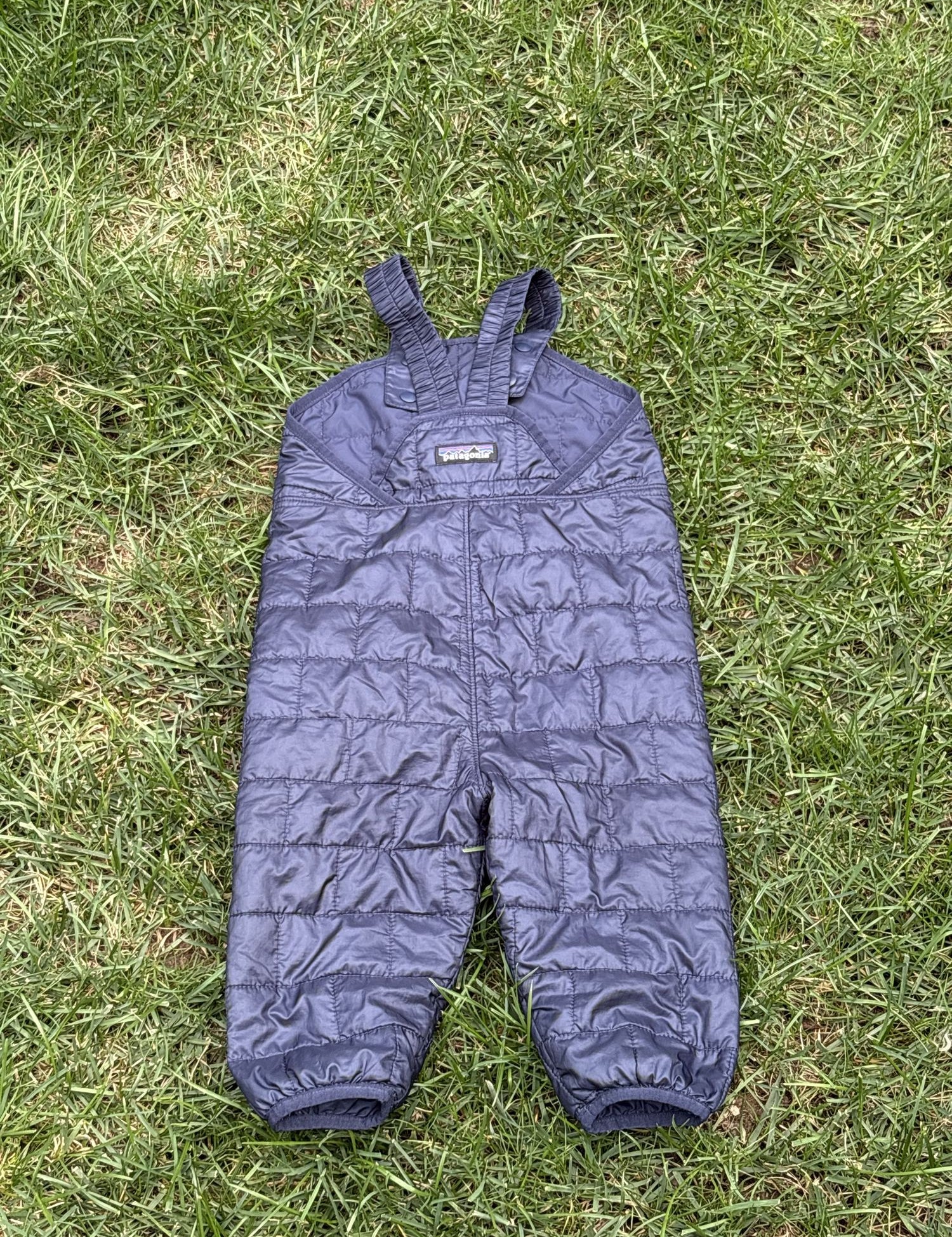 Pre-loved Patagonia navy quilted insulated bib overalls, kids size 12-18M, front view, laid flat on grass
