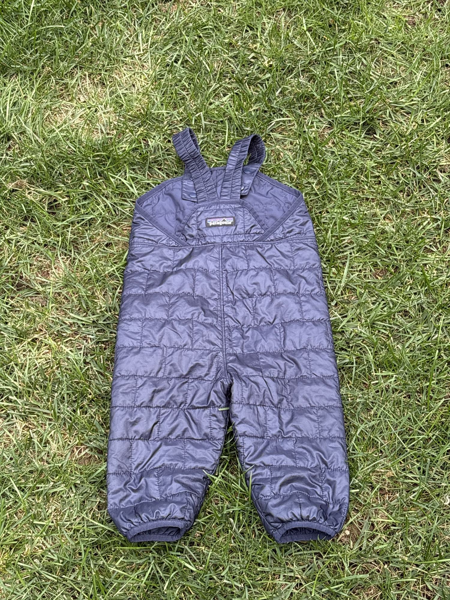 Pre-loved Patagonia navy quilted insulated bib overalls, kids size 12-18M, front view, laid flat on grass