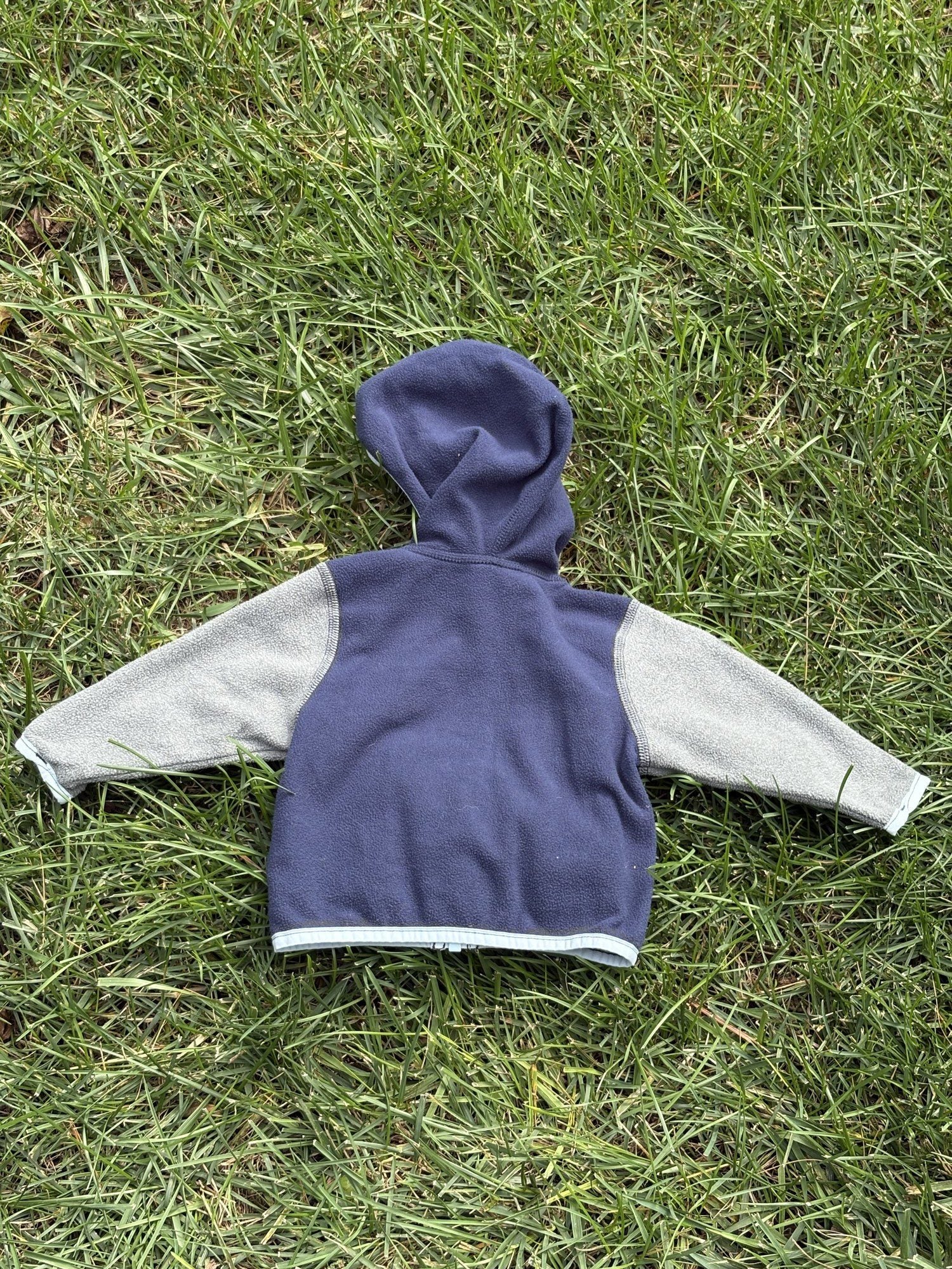 Pre-loved The North Face navy and gray full-zip fleece hoodie, kids size 3-6M, back view, laid flat on grass
