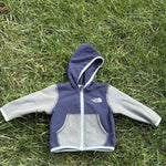 Pre-loved The North Face navy and gray full-zip fleece hoodie, kids size 3-6M, front view, laid flat on grass