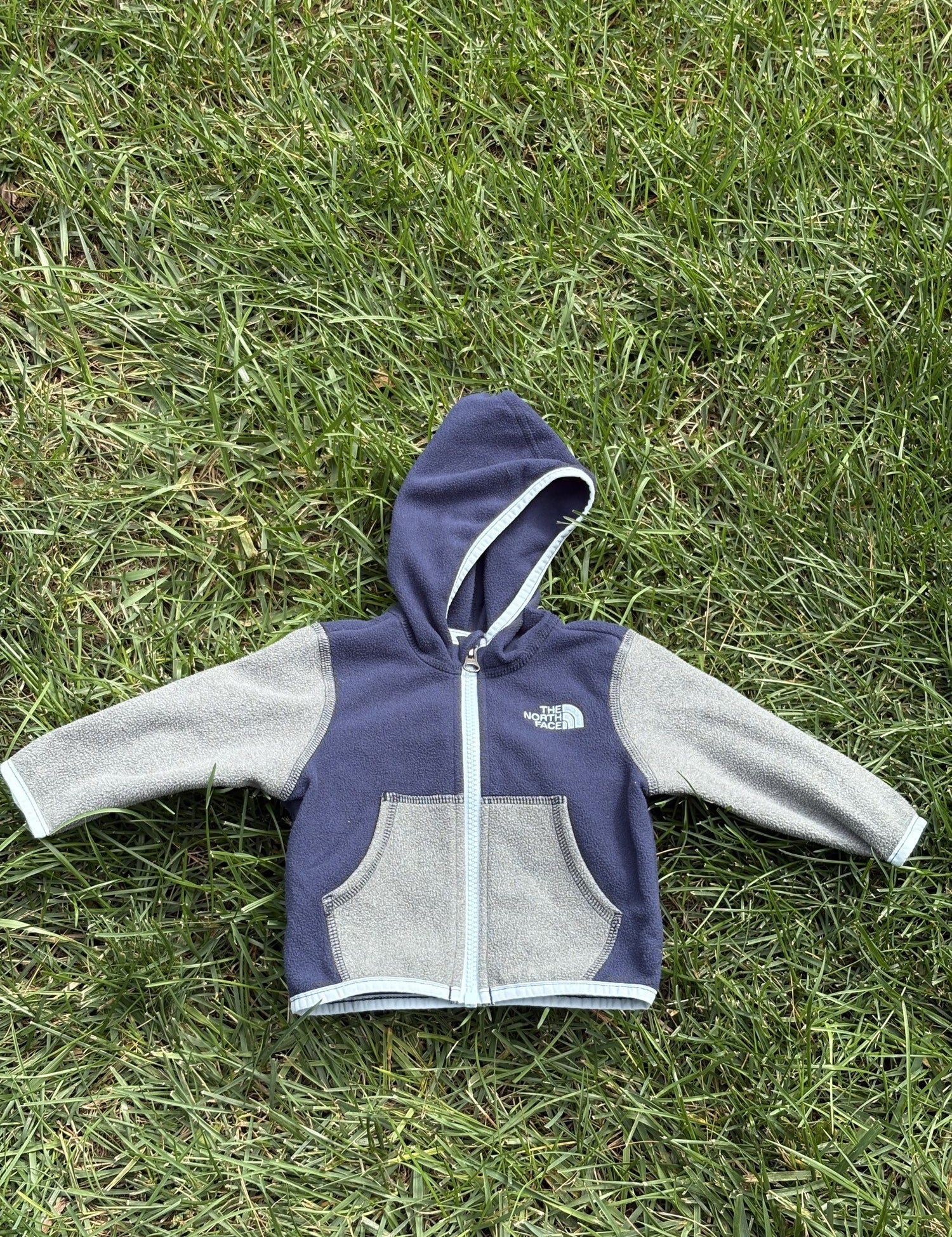 Pre-loved The North Face navy and gray full-zip fleece hoodie, kids size 3-6M, front view, laid flat on grass