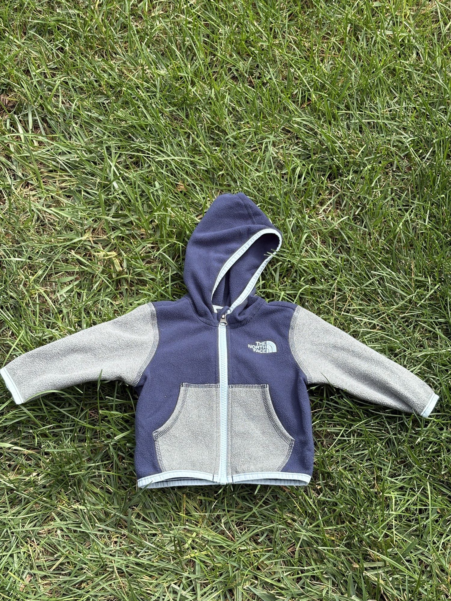 Pre-loved The North Face navy and gray full-zip fleece hoodie, kids size 3-6M, front view, laid flat on grass