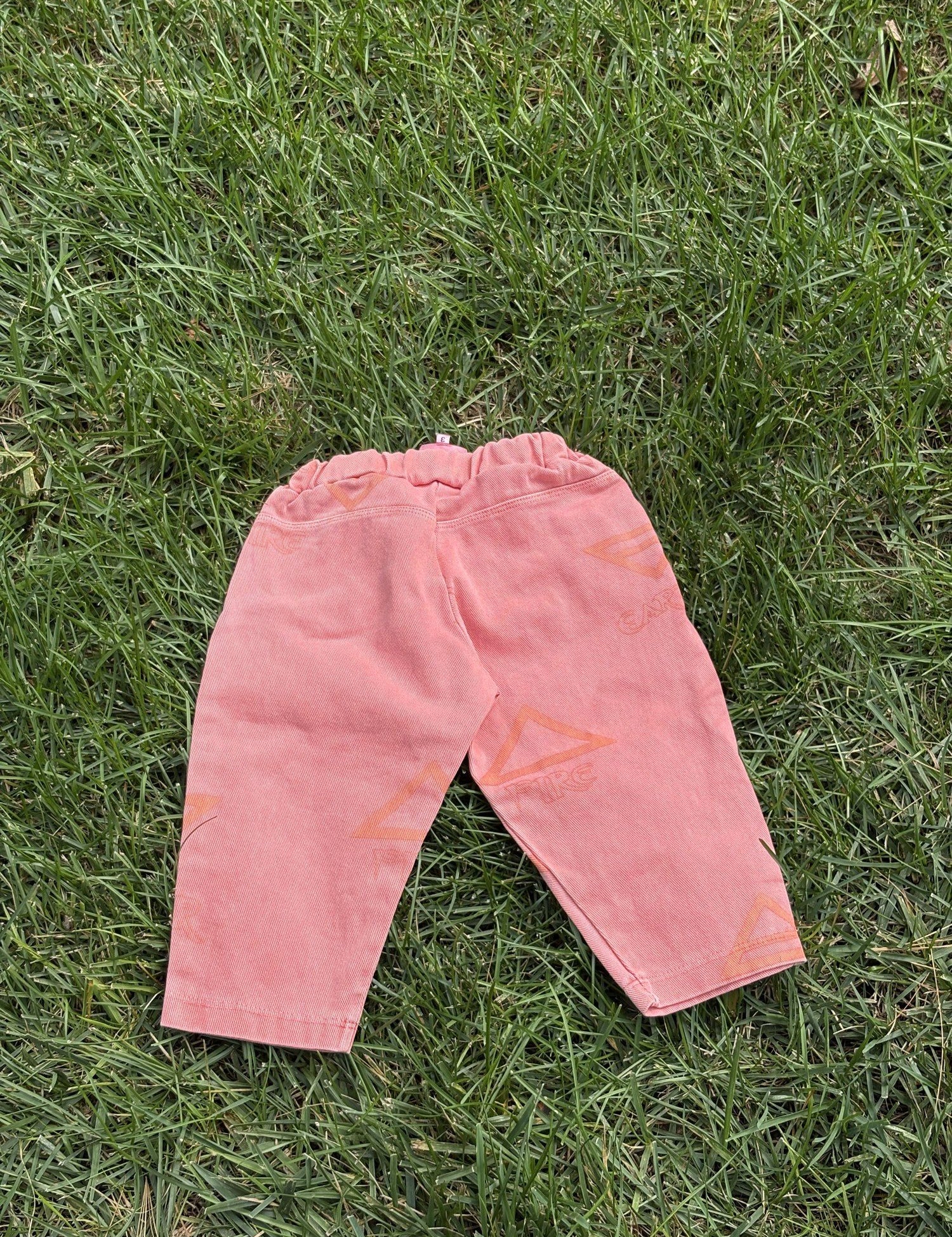 Pre-loved Unbranded coral star print pull-on pants, kids size 3T, back view, laid flat on grass