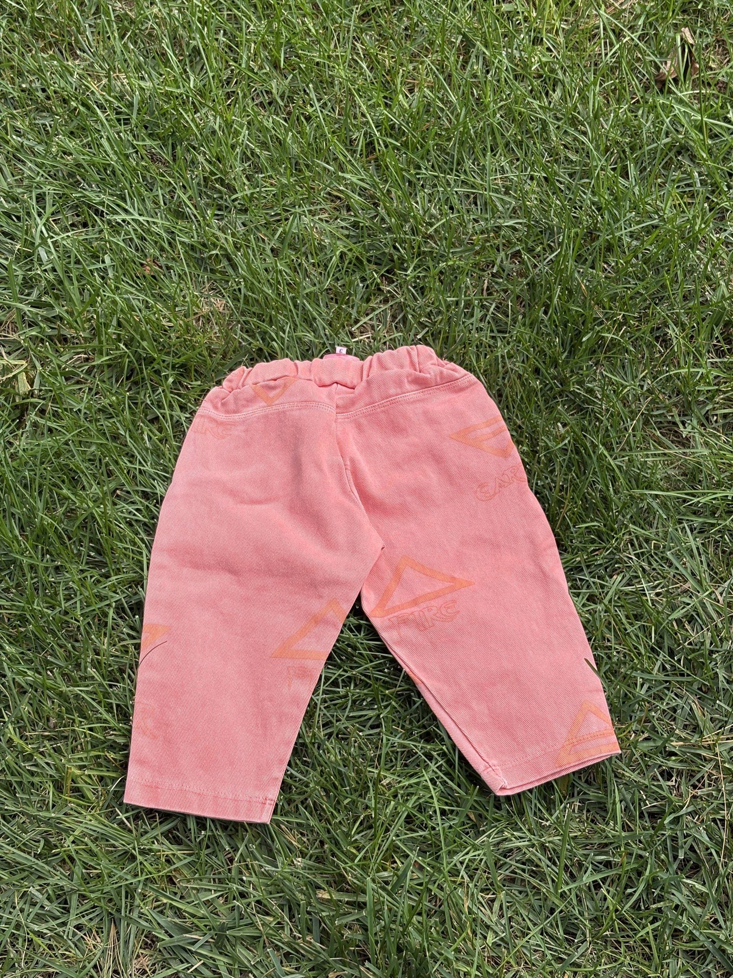 Pre-loved Unbranded coral star print pull-on pants, kids size 3T, back view, laid flat on grass